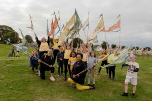 Group of people standing and kneeling on grass each holding a silk flag pennant