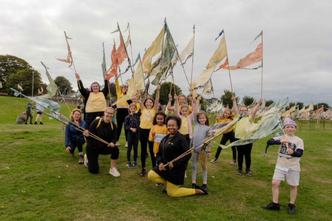 Group of people standing and kneeling on grass each holding a silk flag pennant