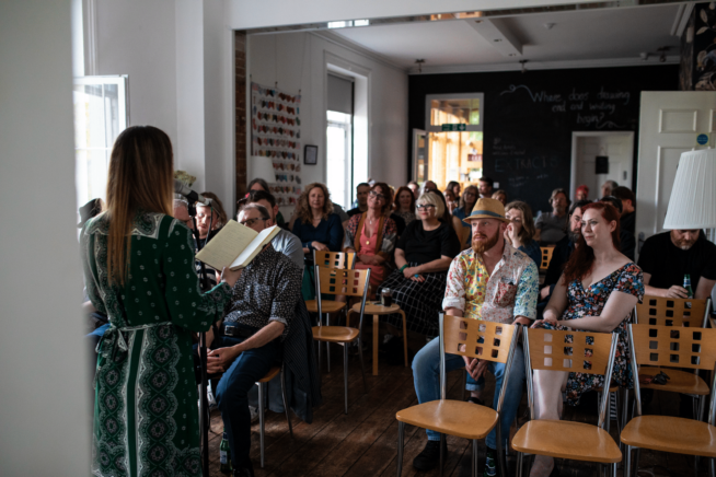 Person standing at microphone reading from a notepad in front of a seated audience