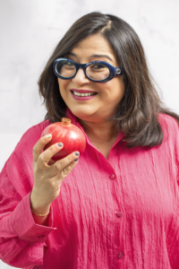 Photo of Radhika Howarth in a bright pink top holding a pomegranate.