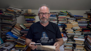 Photo of Robin Ince surrounded by piles of books