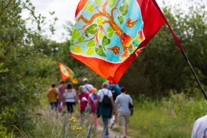 People walking outide along a grassy path holding brightly coloured flags