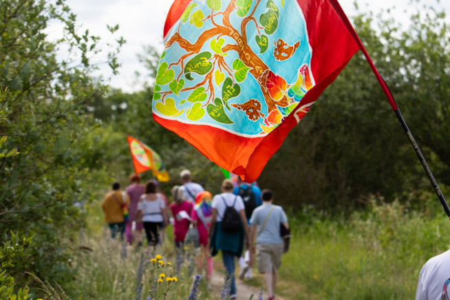 People walking outide along a grassy path holding brightly coloured flags
